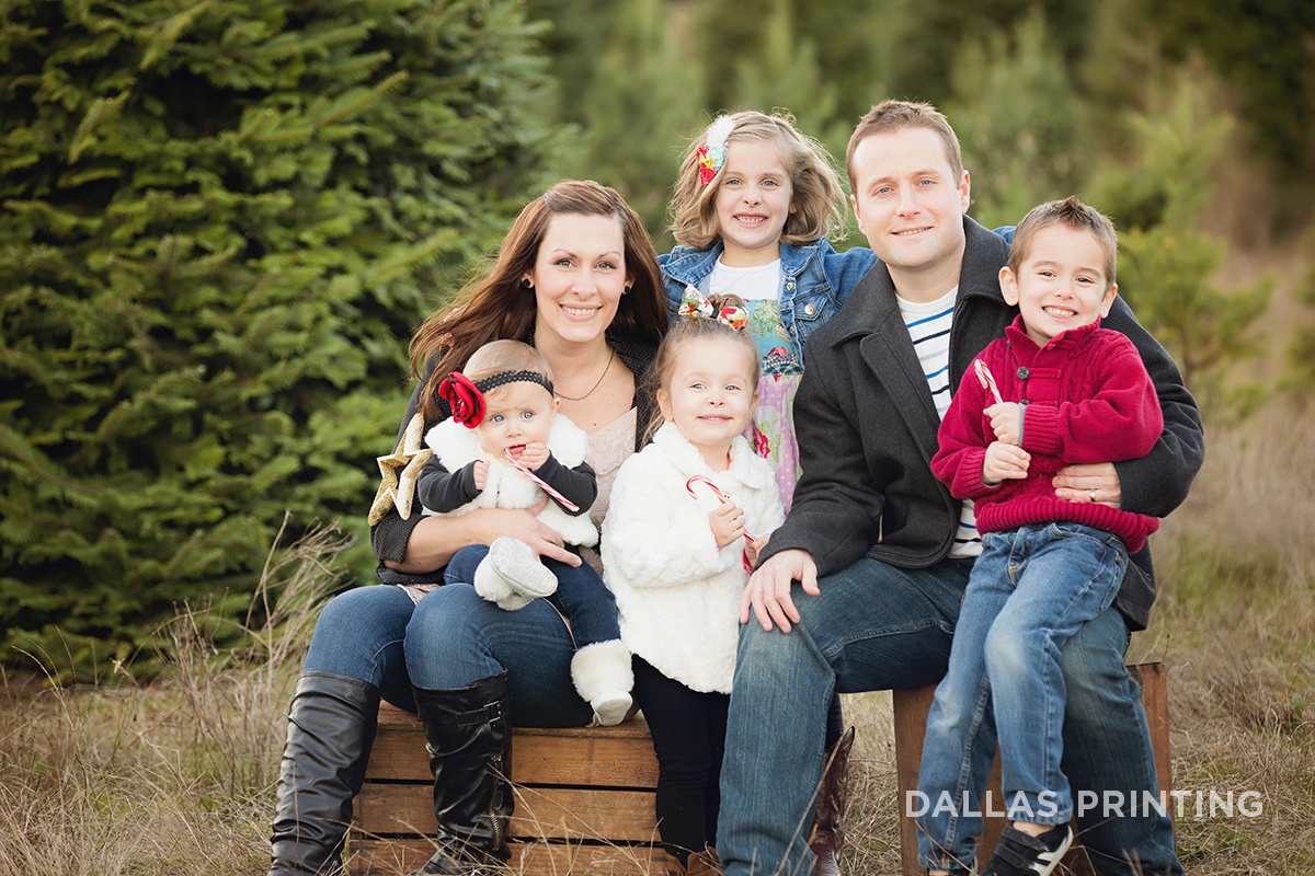Young family with 4 children poses for holiday photo in Christmas Tree Farm. Happy and smiling.